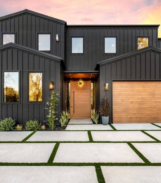 Modern black house exterior with wooden garage door and driveway at sunset.