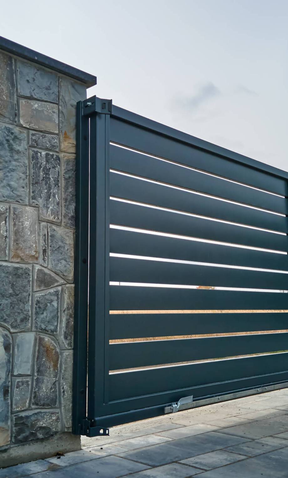 Wide automatic sliding gate with remote control installed in high stone fense wall. Security and protection concept.